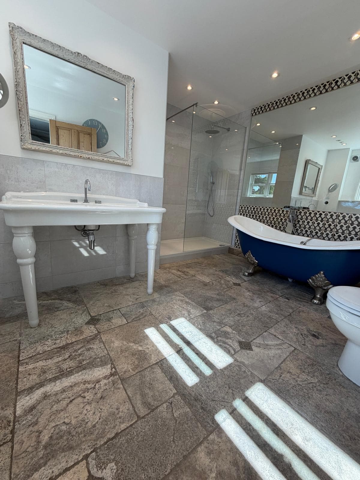 Bathroom renovation with a navy roll-top freestanding bath, walk-in glass shower and stone-effect tiled floor